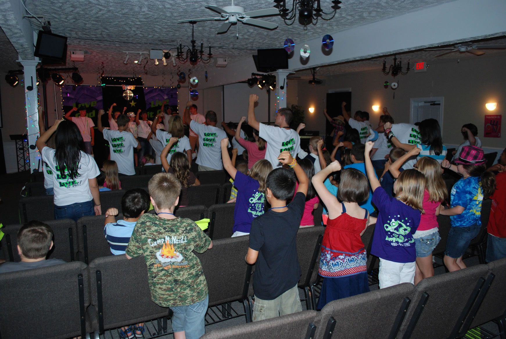 A group of children are dancing in a room with the number 111 on their shirts