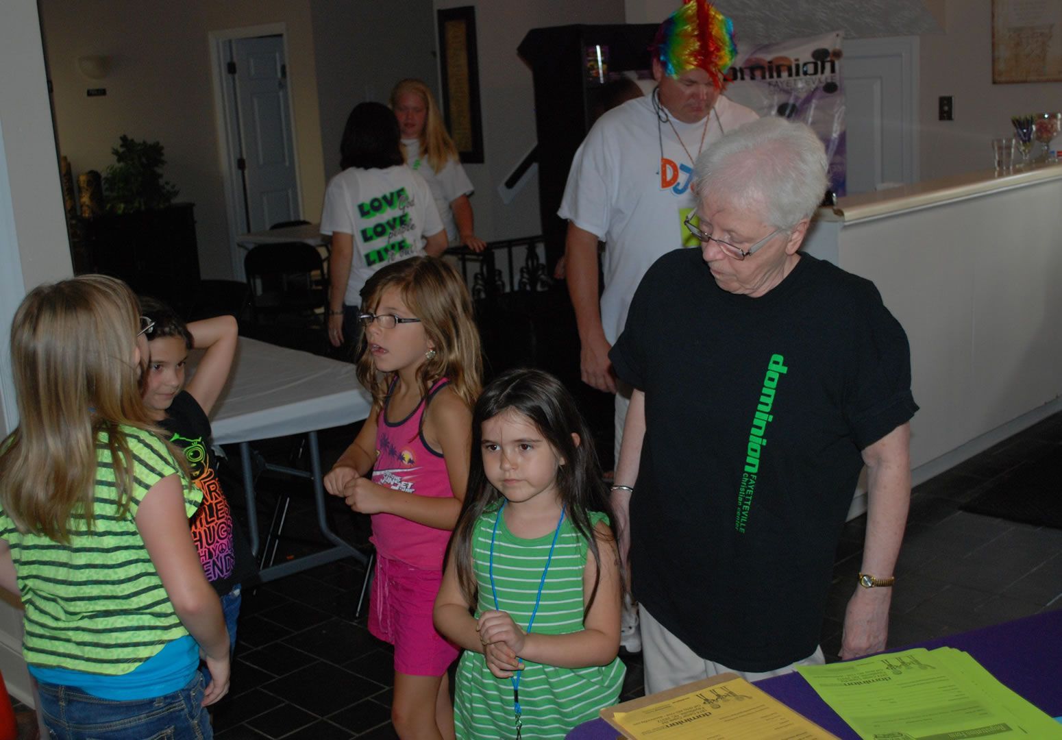 A group of young girls are standing around a table with a woman wearing a black shirt that says alzheimer 's