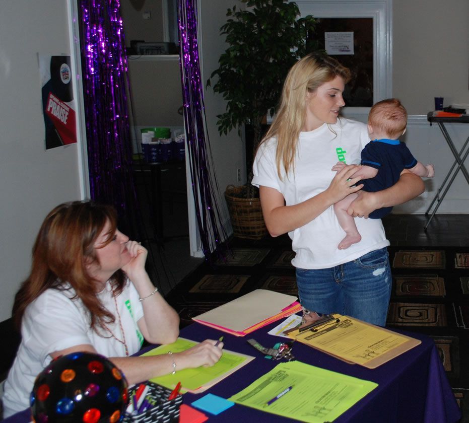 A woman is holding a baby while another woman sits at a table