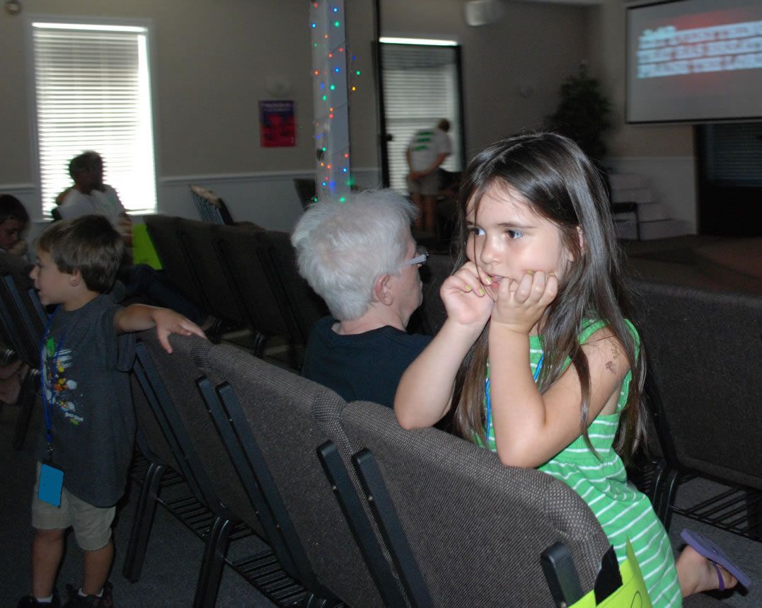 A little girl in a green dress sits in a chair