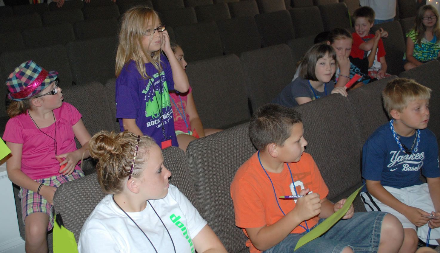 A group of children are sitting in a theater watching a presentation