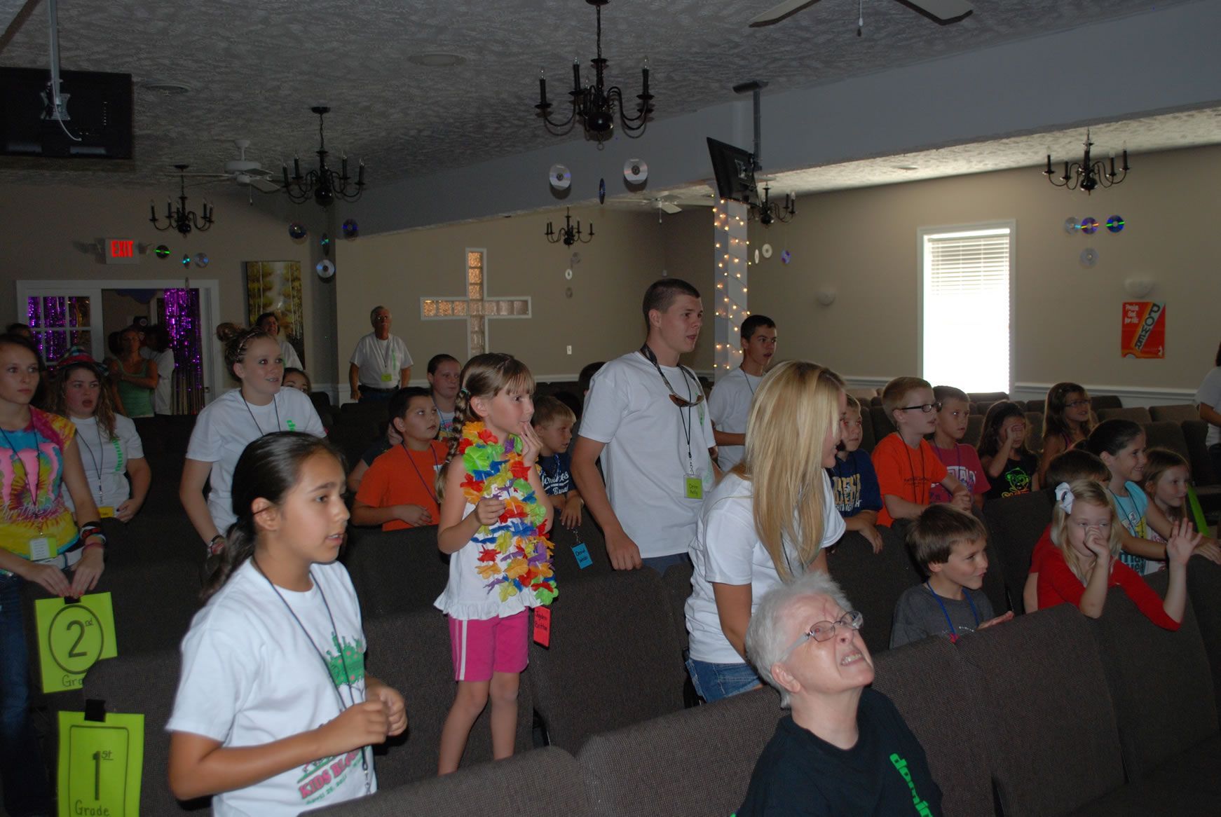 A group of people are standing in a room with a cross on the wall.
