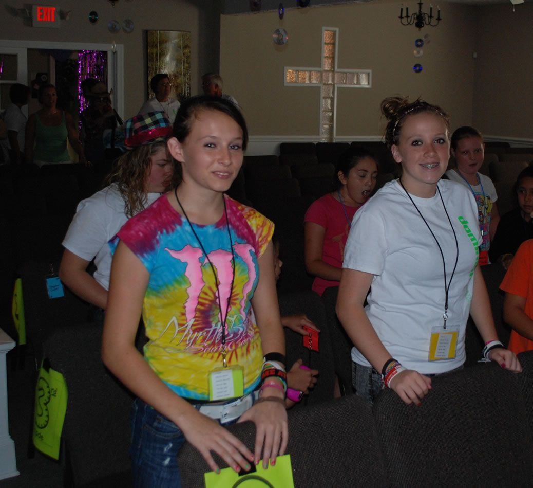 A group of girls are standing in a room with a cross on the wall
