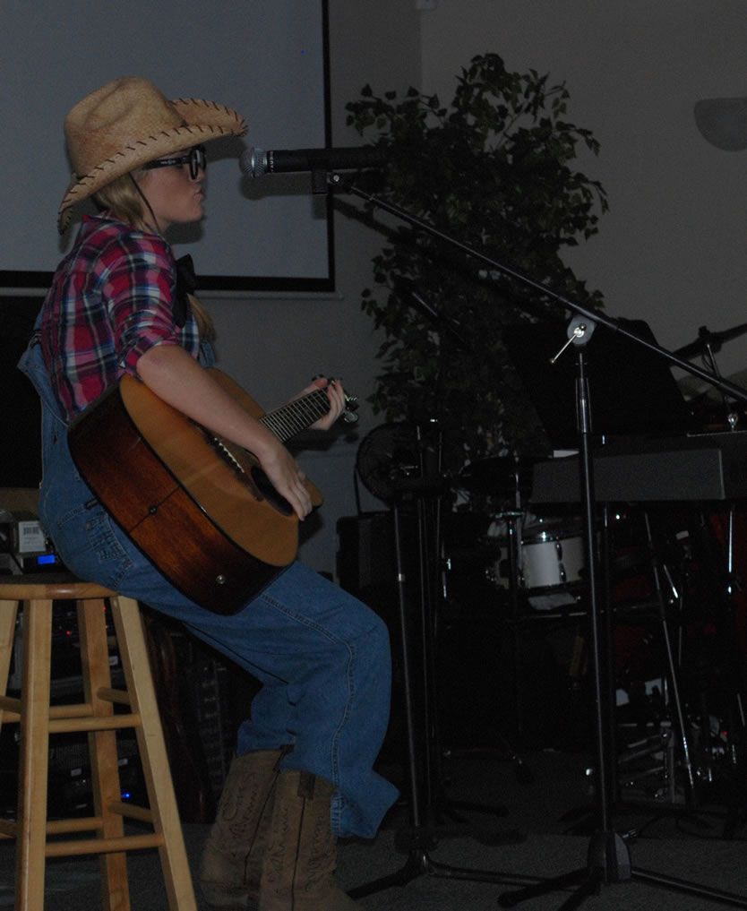 A woman in a cowboy hat is sitting on a stool playing a guitar