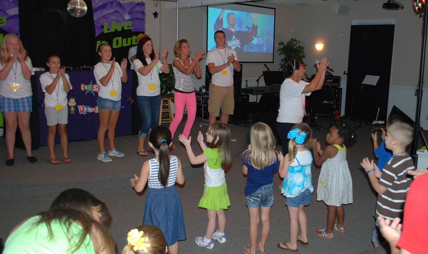 A group of children are dancing in front of a projector screen that says 