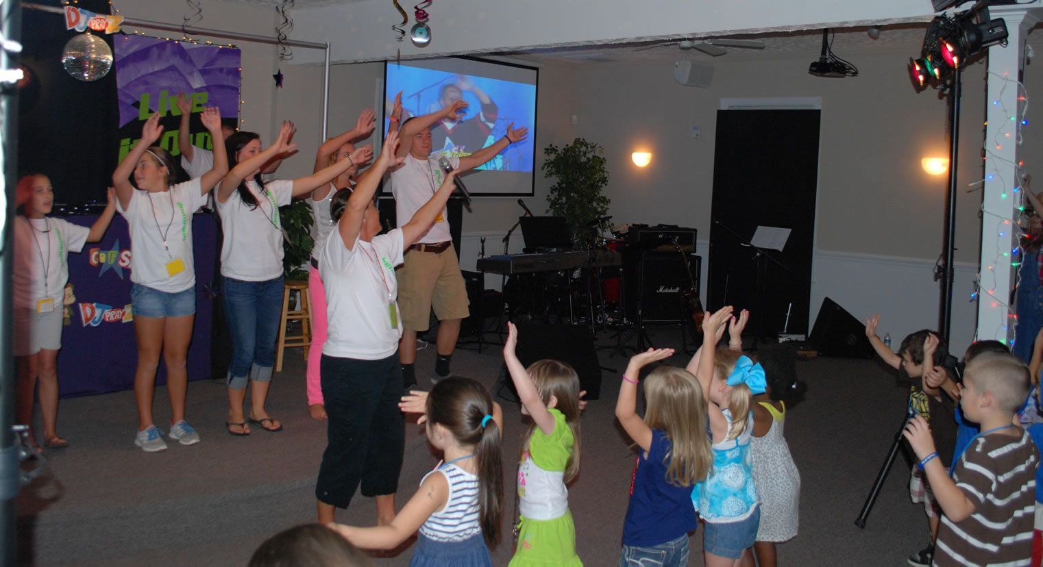 A group of children are dancing in a room with a projector screen in the background