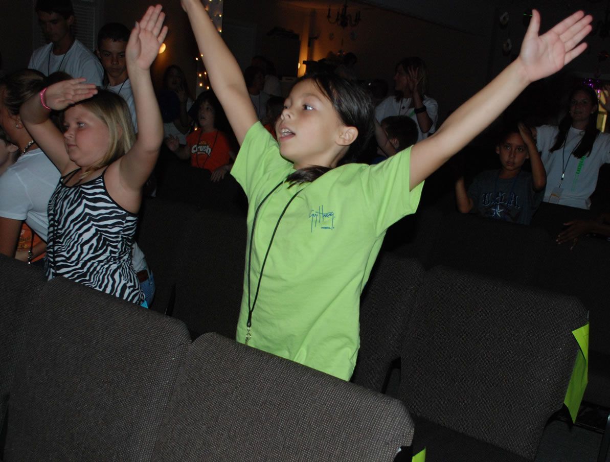 A girl in a green shirt is raising her arms in the air