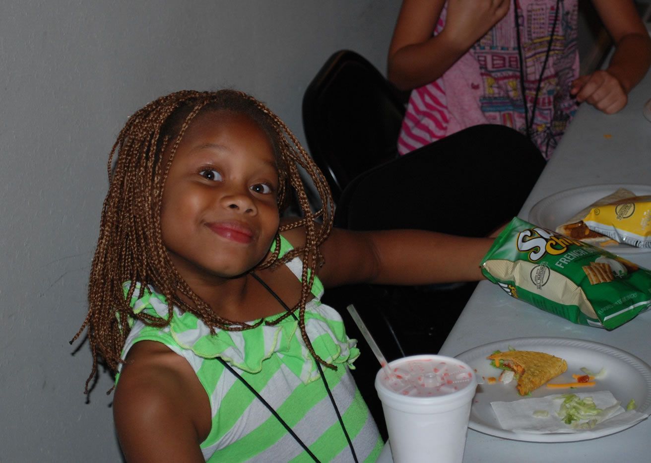 A little girl sitting at a table with a bag of pringles chips
