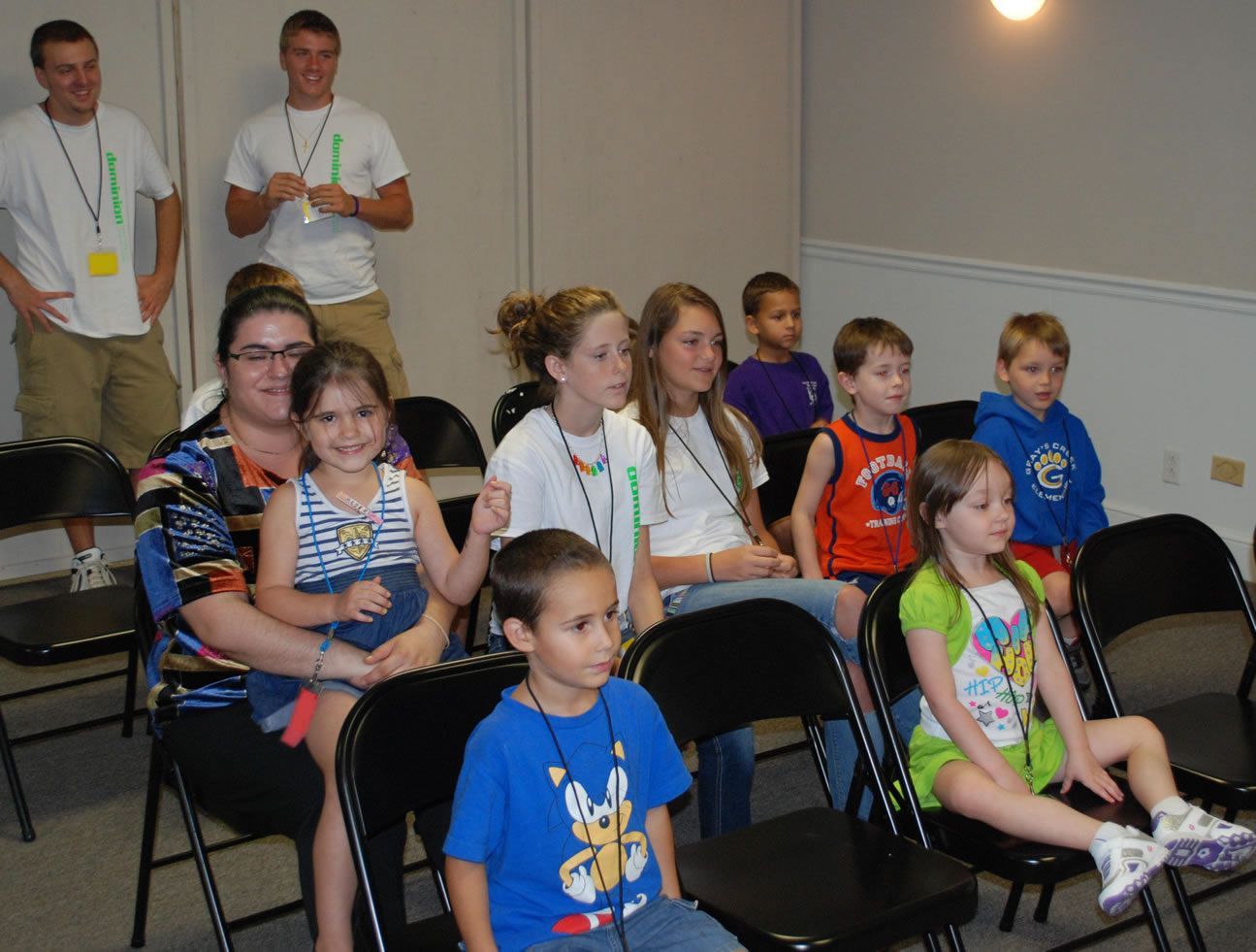 A group of children are sitting in folding chairs in a room