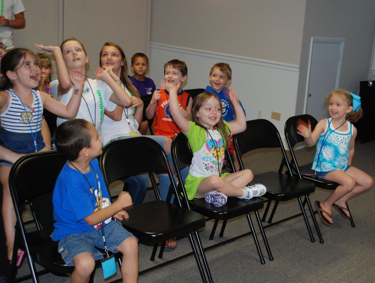 A group of children are sitting in chairs with their hands in the air