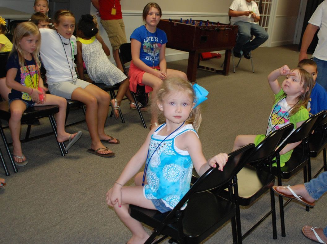 A group of children are sitting in chairs in a room with a foosball table in the background