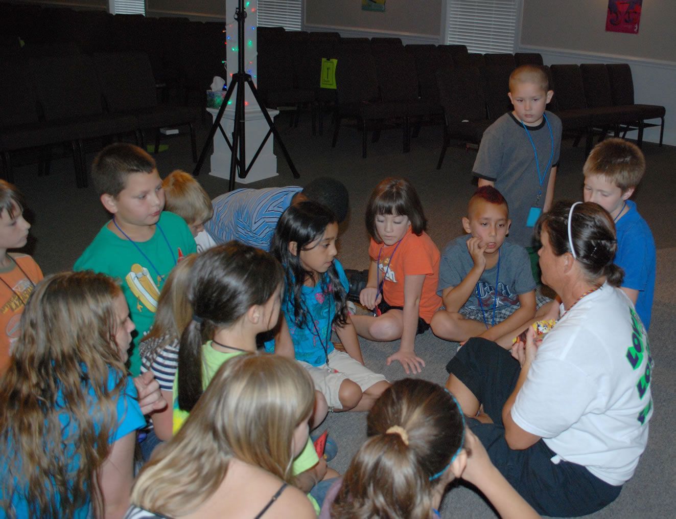 A group of children are sitting in a circle with a woman talking to them.
