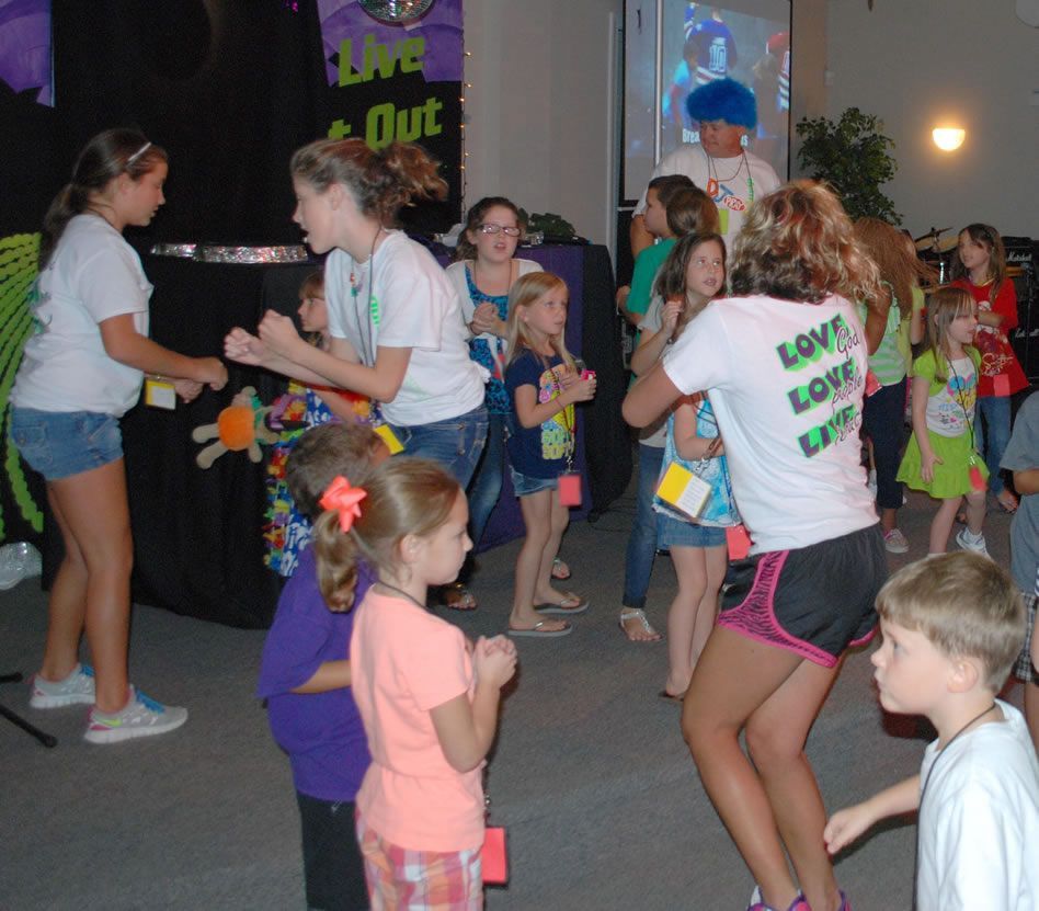 A group of children are dancing in front of a sign that says live and out