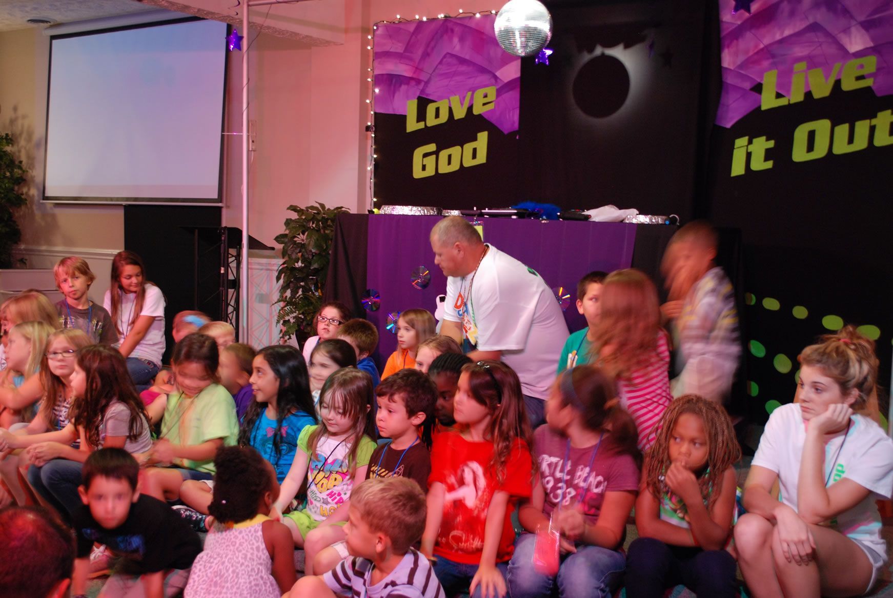 A group of children are sitting in front of a sign that says love god
