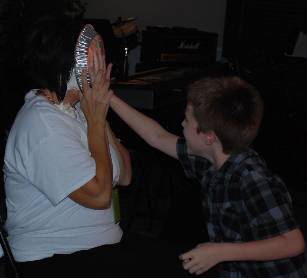 A young boy is putting a pie in a woman 's face