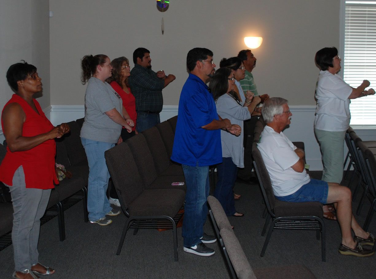 A group of people are standing and sitting in chairs in a room