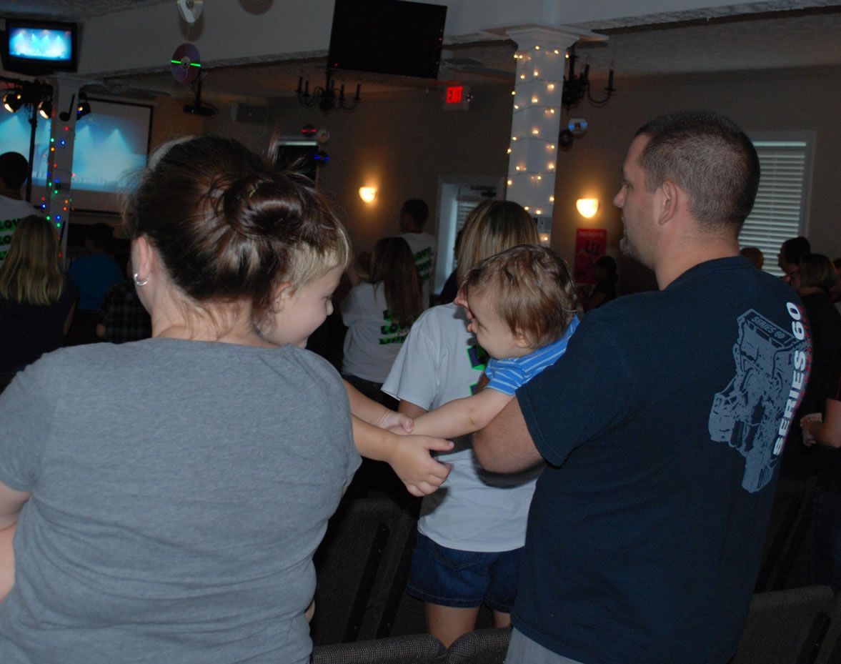 A man in a maverick 80 shirt is holding a baby