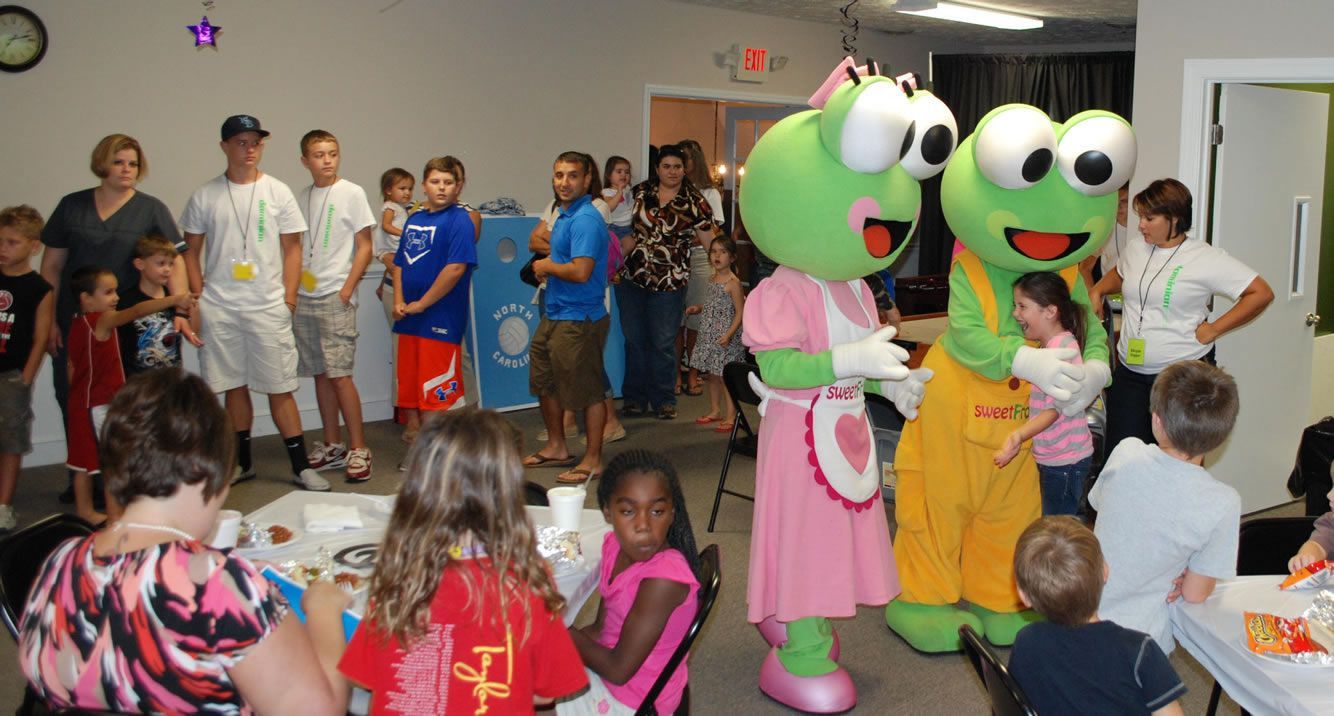 A group of children are sitting at a table with frog mascots