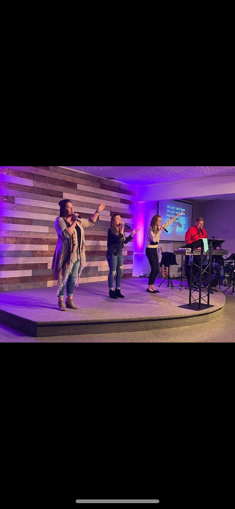 A group of people are standing on a stage singing into microphones.