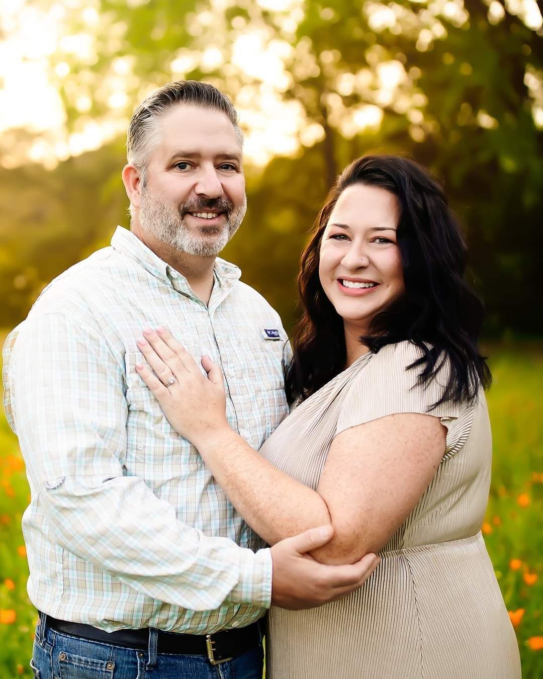 A man and a woman are posing for a picture in a field of flowers.