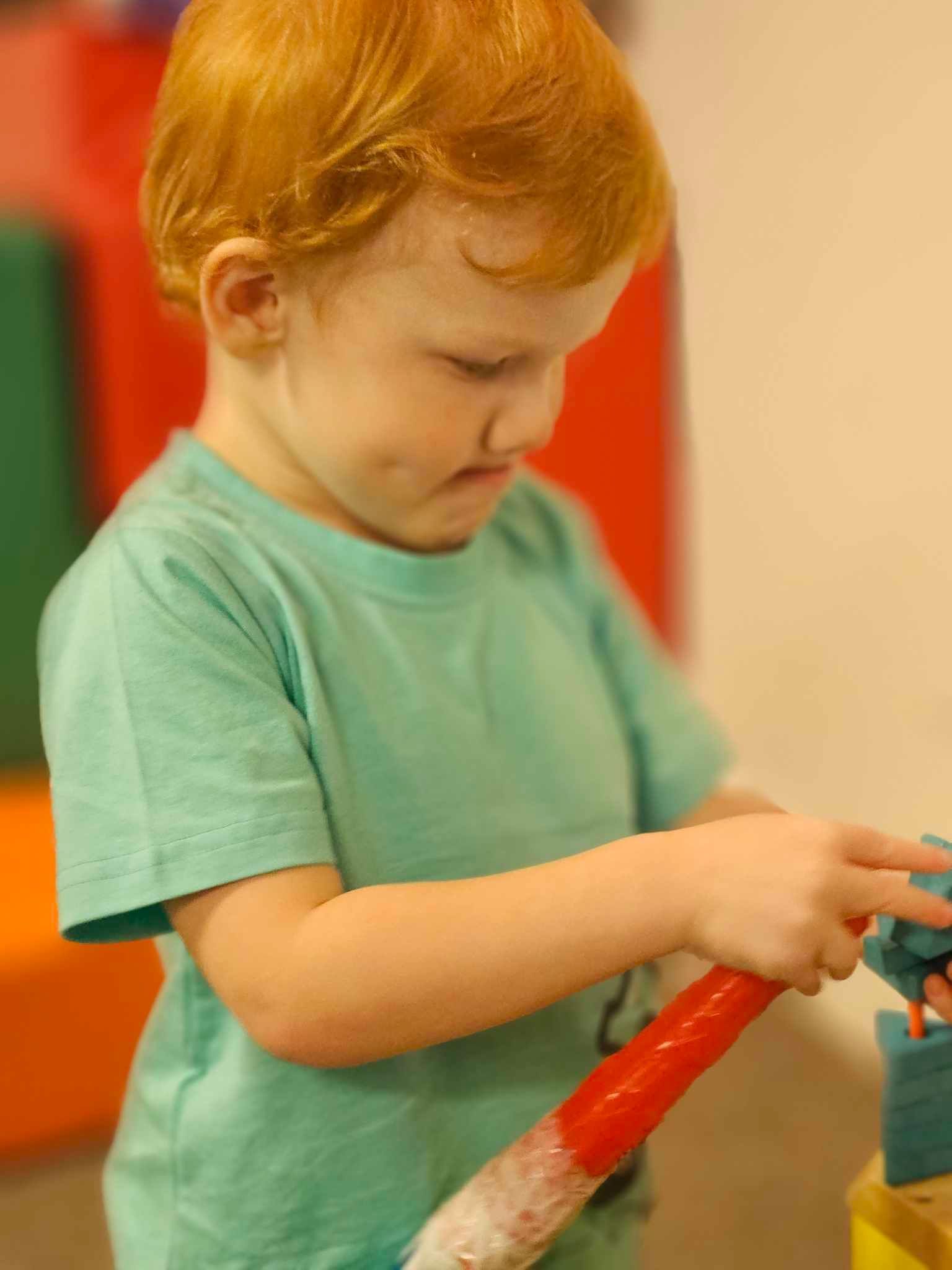 A young boy with red hair is playing with a red stick.