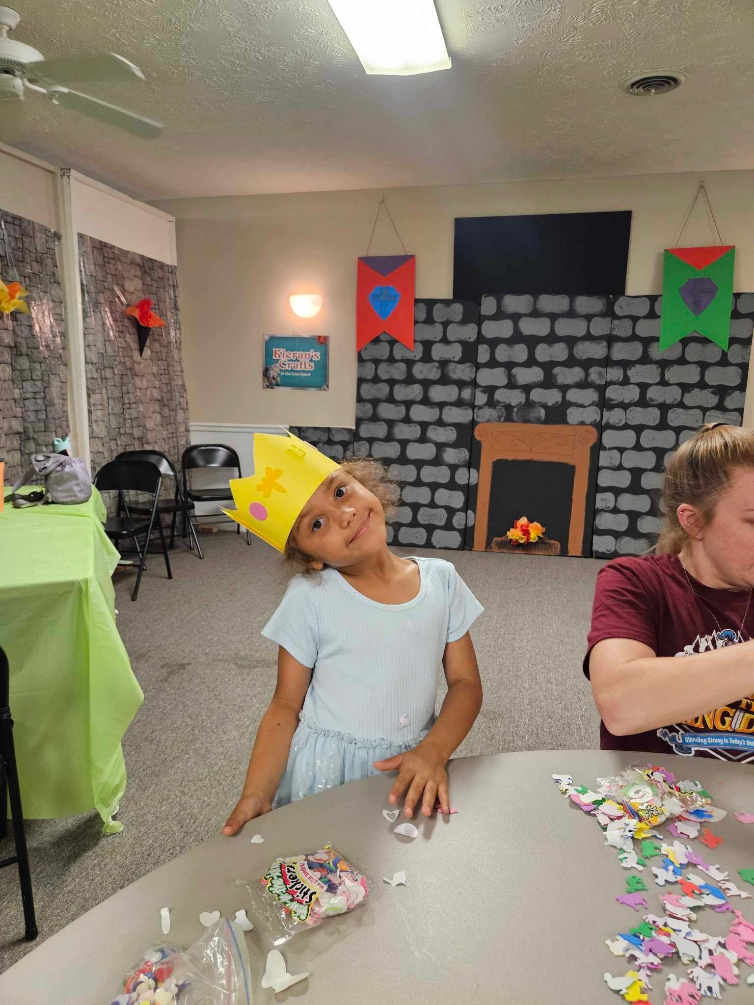 A little girl wearing a crown is sitting at a table with puzzles.