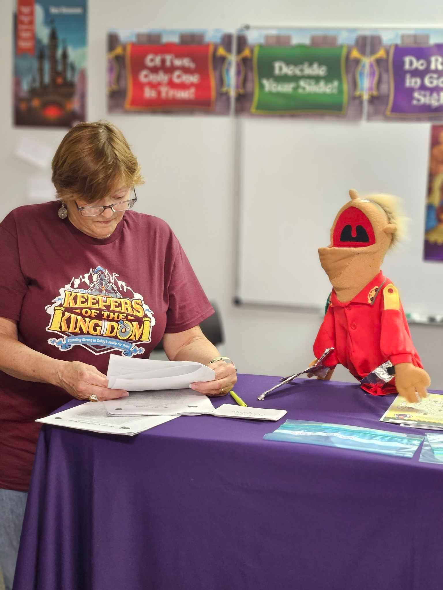 A woman is sitting at a table with a puppet on it.