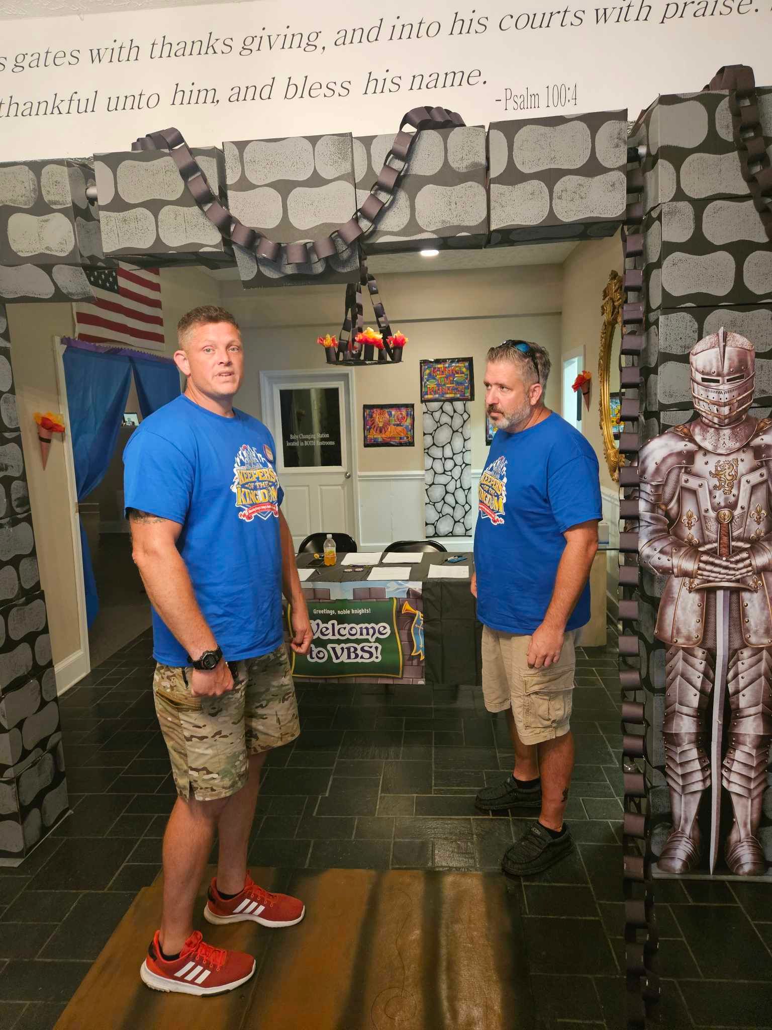 Two men in blue shirts are standing next to each other in a room.