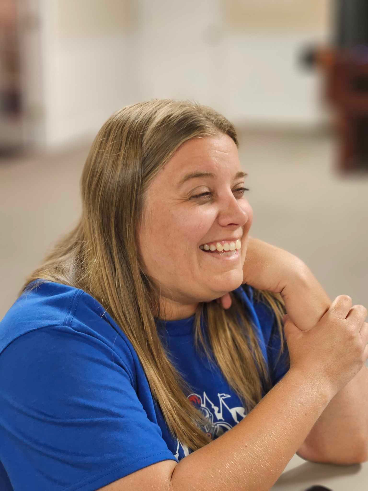 A woman in a blue shirt is smiling while sitting at a table.