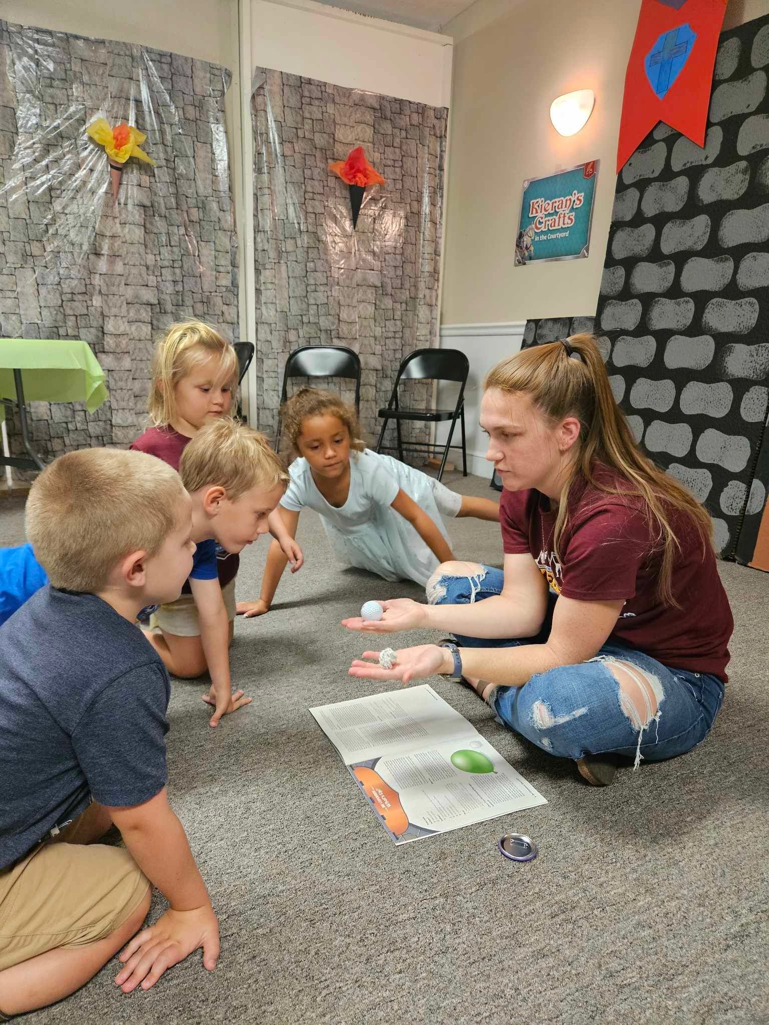 A woman is sitting on the floor talking to a group of children.