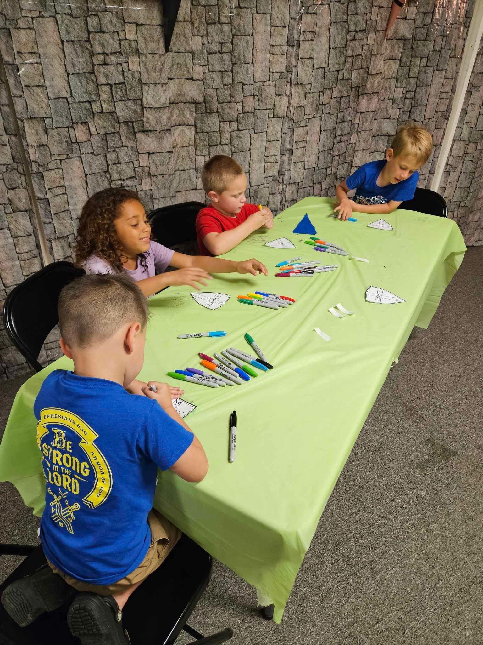 A group of children are sitting at a table with markers.