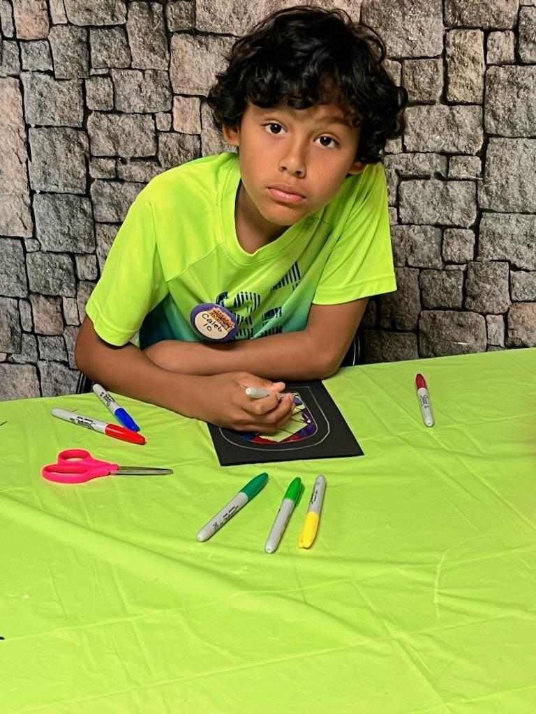 A young boy is sitting at a table with scissors and markers.