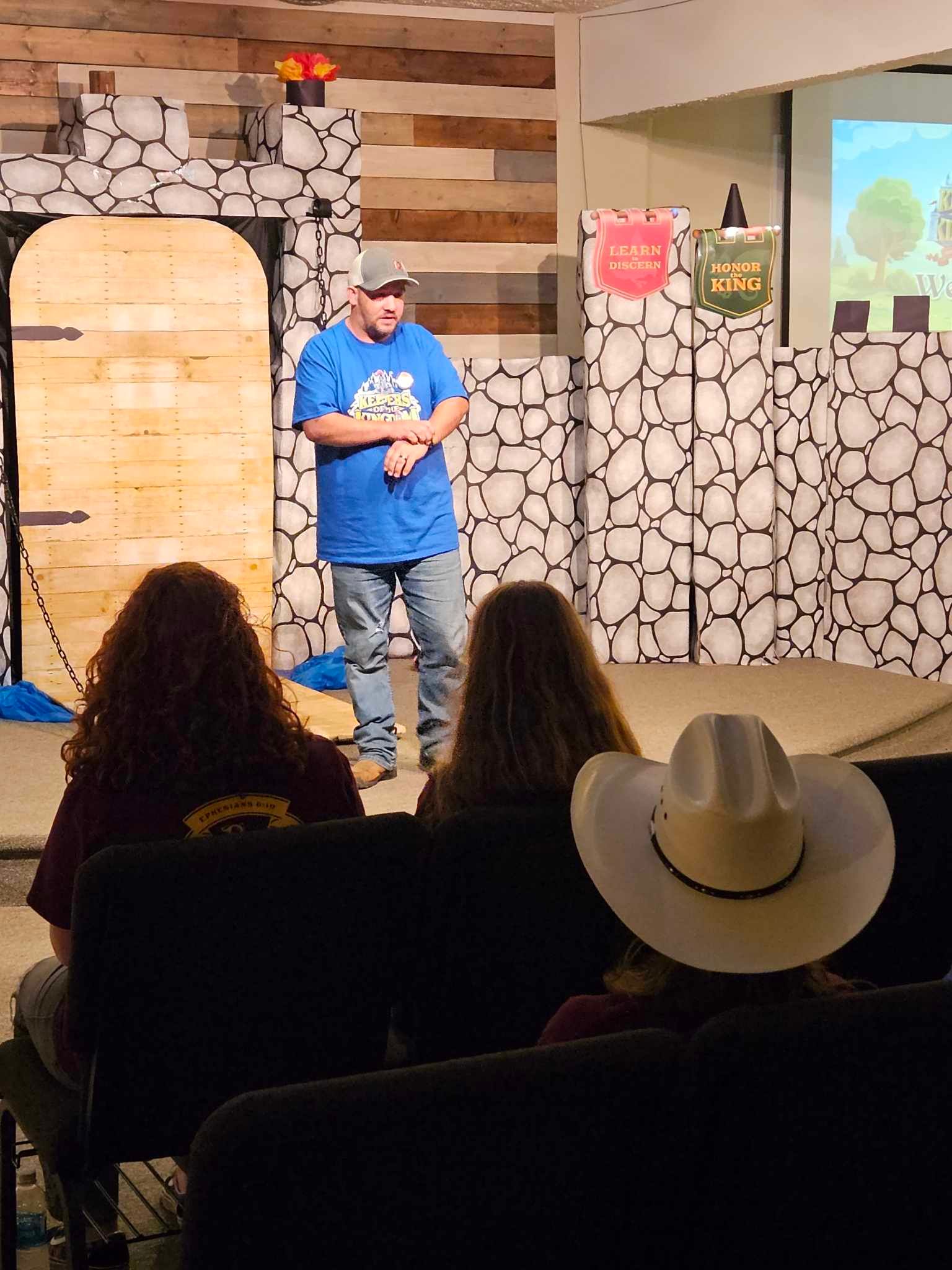 A man in a blue shirt is standing in front of a group of people wearing cowboy hats.