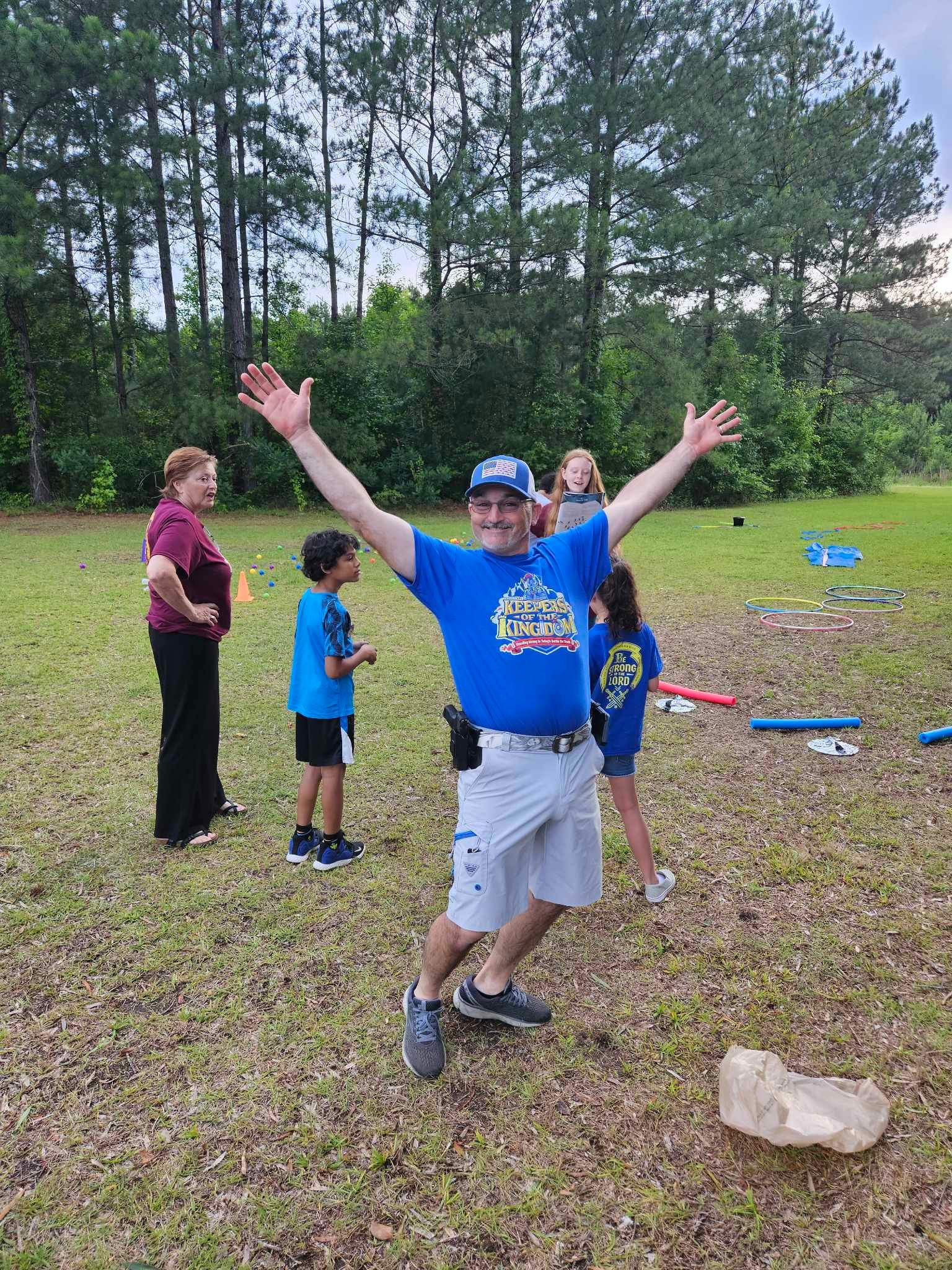 A man in a blue shirt is standing in a field with his arms outstretched.