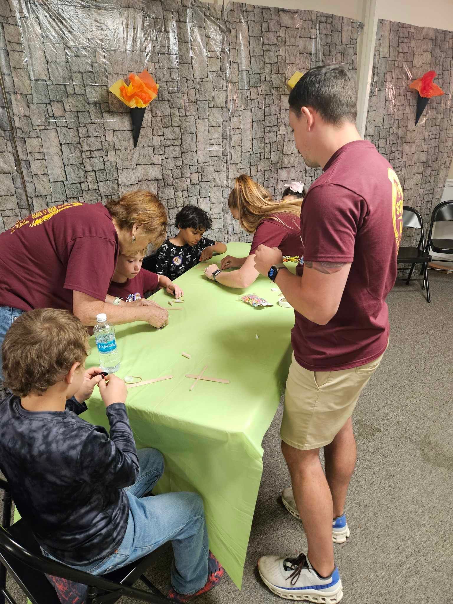 A group of children are sitting at a table with a man standing next to them.