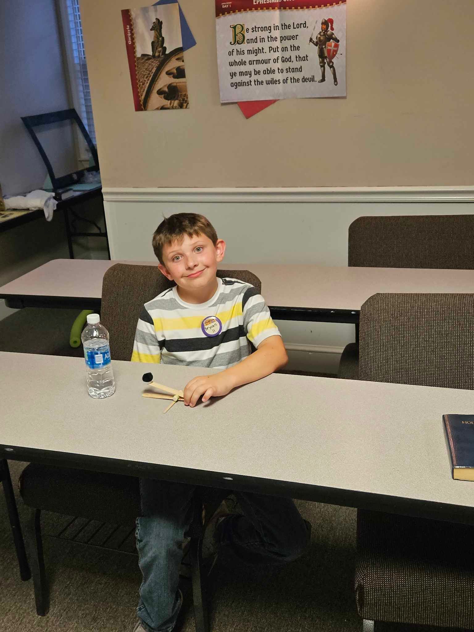 A young boy is sitting at a table with a water bottle on it.
