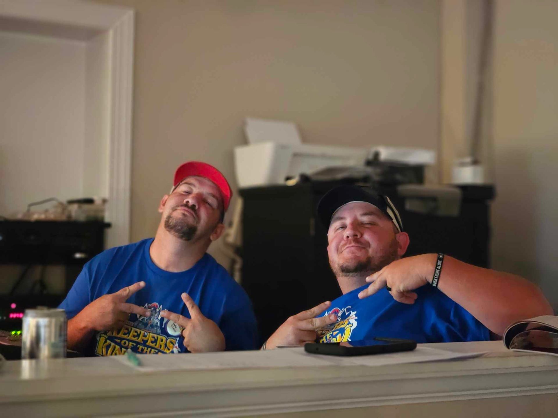 Two men are sitting at a table with their hands in the air.