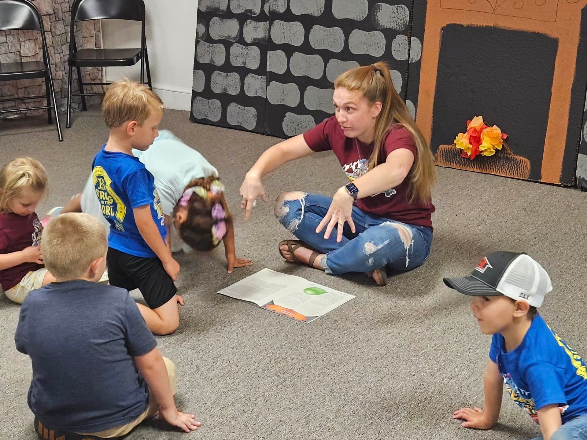 A woman is sitting on the floor reading a book to a group of children.
