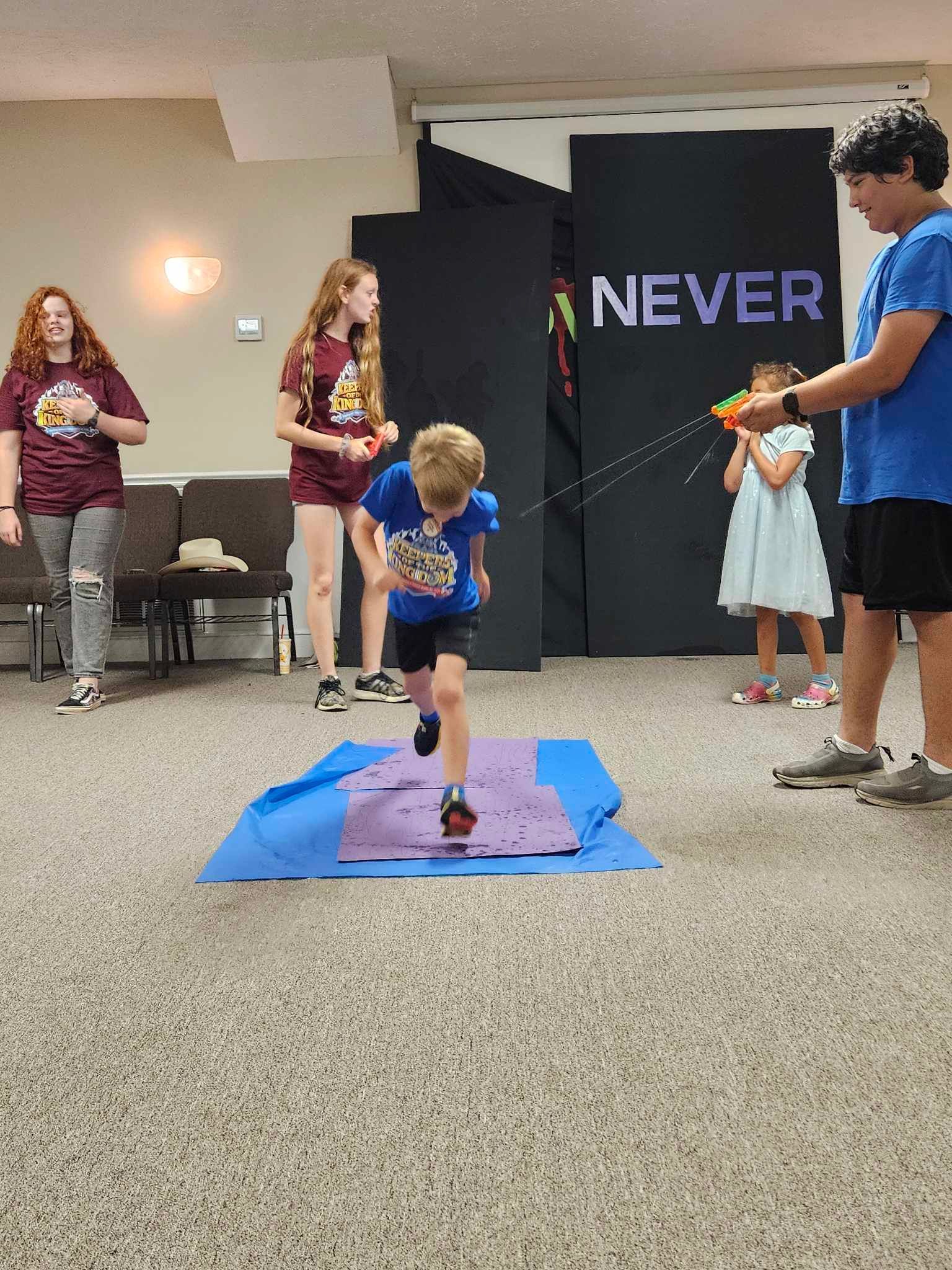 A group of children are playing a game in a room with a sign that says never.