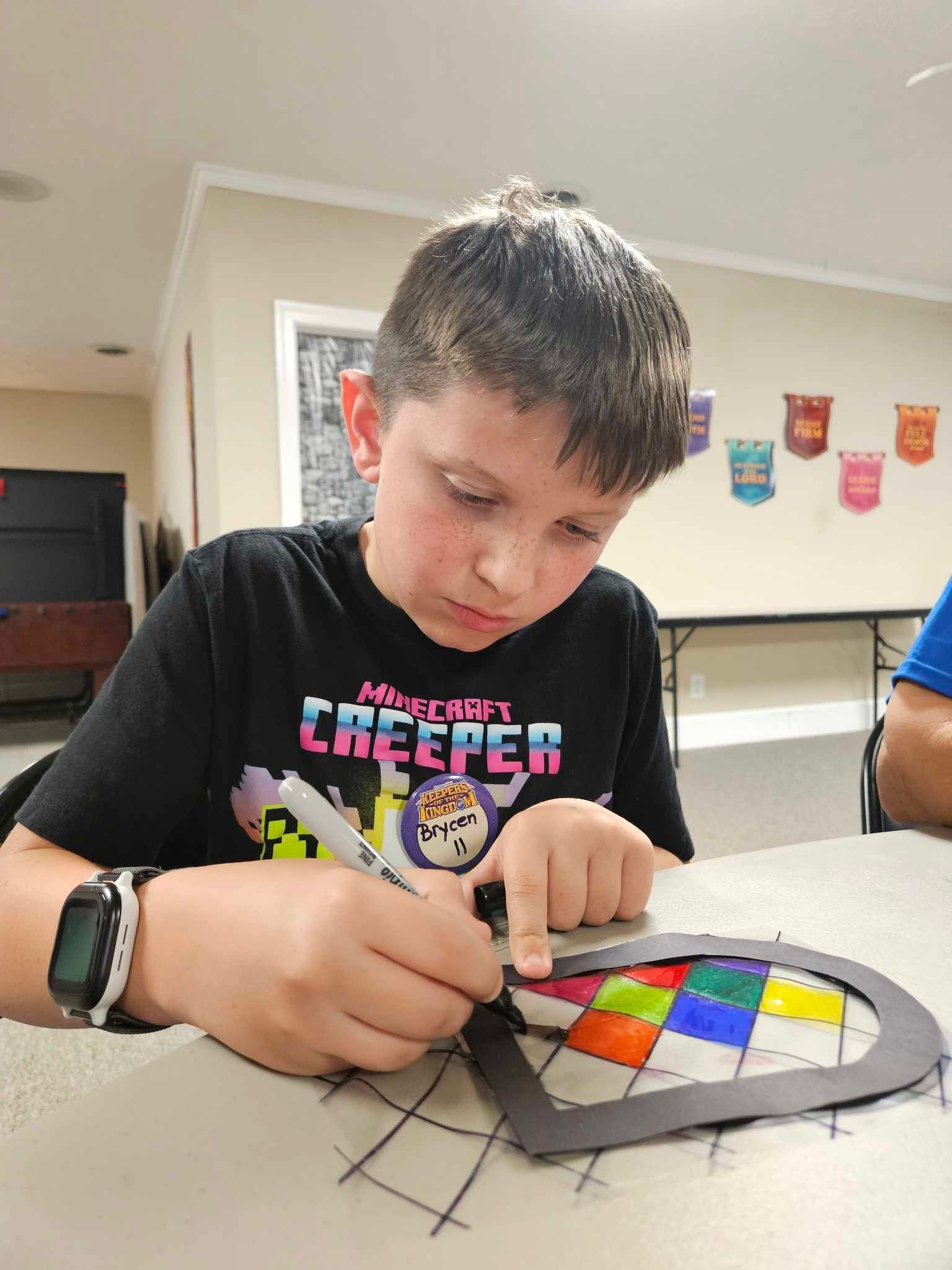 A young boy is sitting at a table writing on a piece of paper.