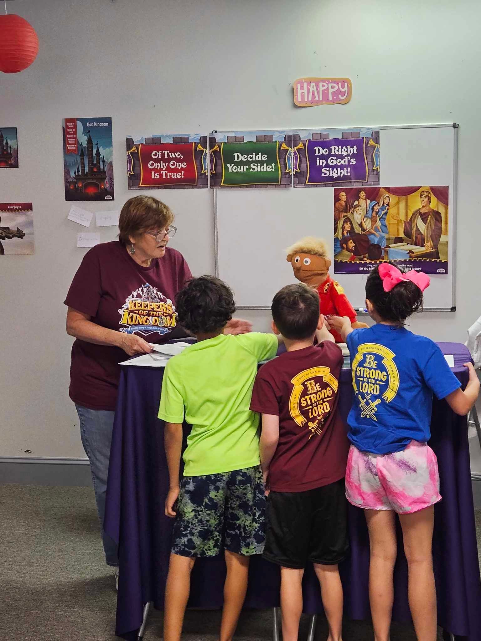 A group of children are standing around a table in front of a sign that says happy day