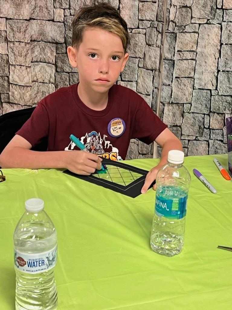 A young boy is sitting at a table with a bottle of water.