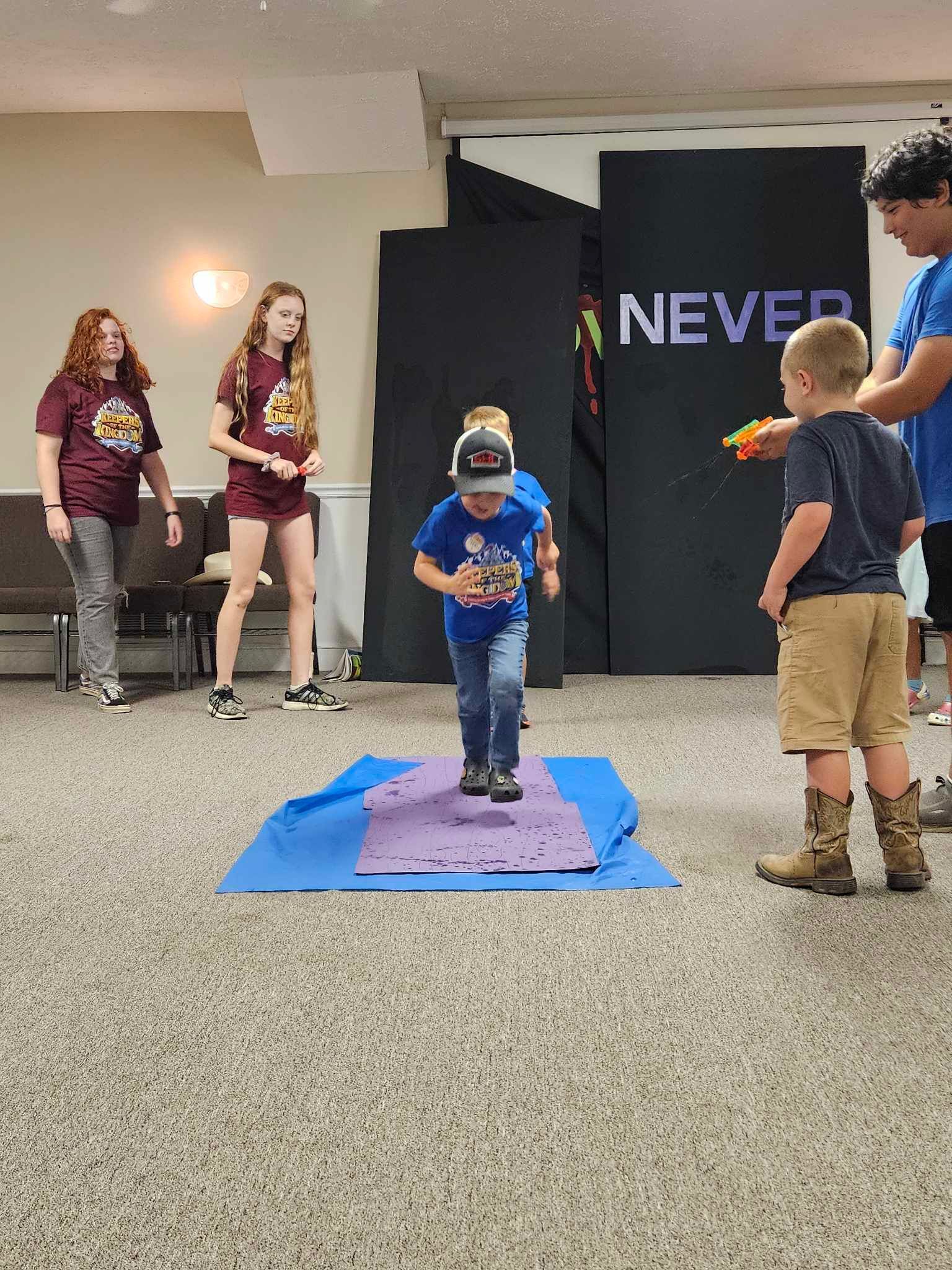 A group of children are playing a game in a room with a sign that says never.