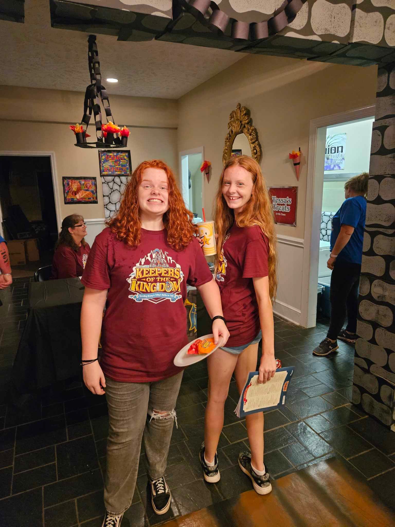 Two girls wearing maroon shirts are standing next to each other in a room.