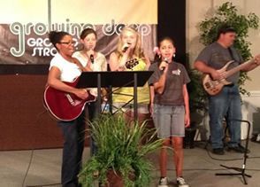A group of people singing and playing guitars in front of a sign that says growing deep