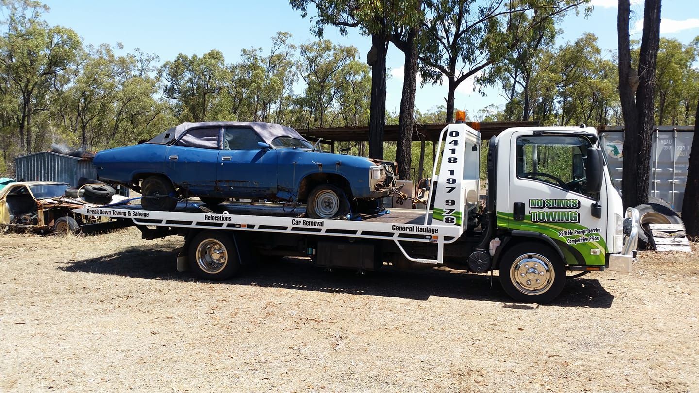 A Blue Car is Towed on a Flatbed Truck in a Dusty Outdoor Setting — No Slings Towing in Glendale, QLD