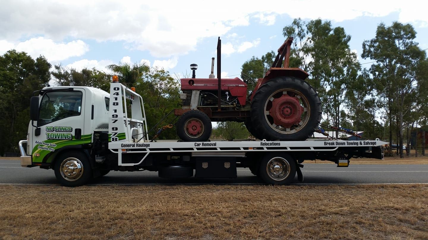 Tow Truck Carrying a Red Tractor on a Flatbed, Roadside Setting — No Slings Towing in Glendale, QLD