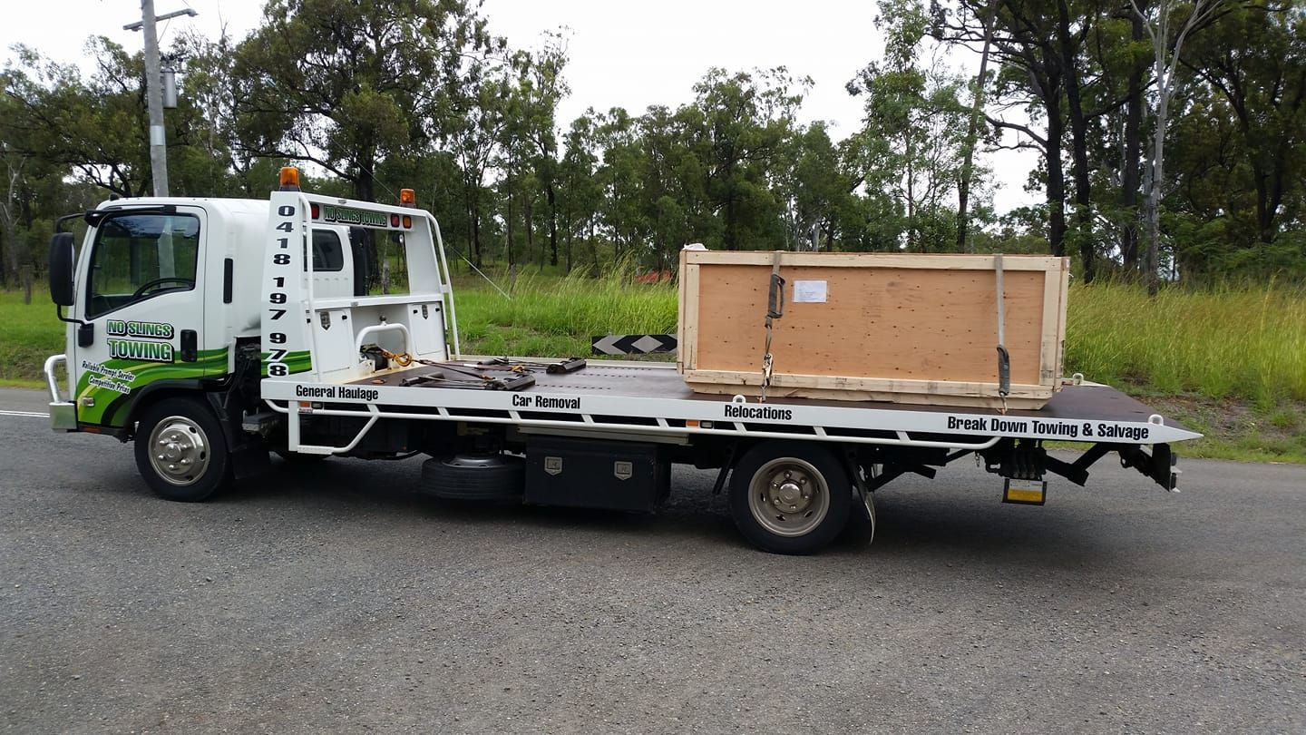 A Flatbed Tow Truck Transporting a Large Wooden Crate on a Roadside — No Slings Towing in Glendale, QLD