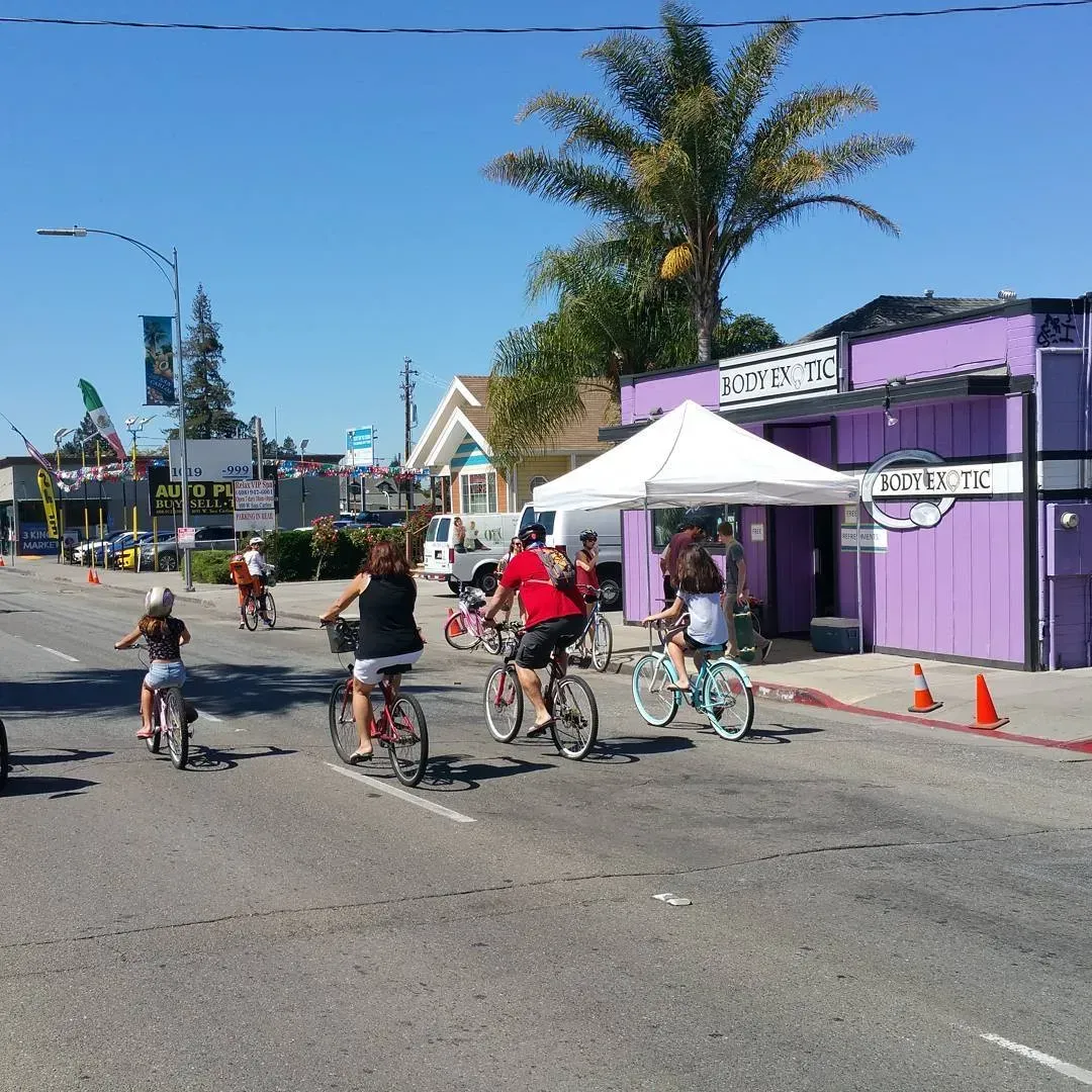 A group of people riding bikes down a street in front of a purple building that says city
