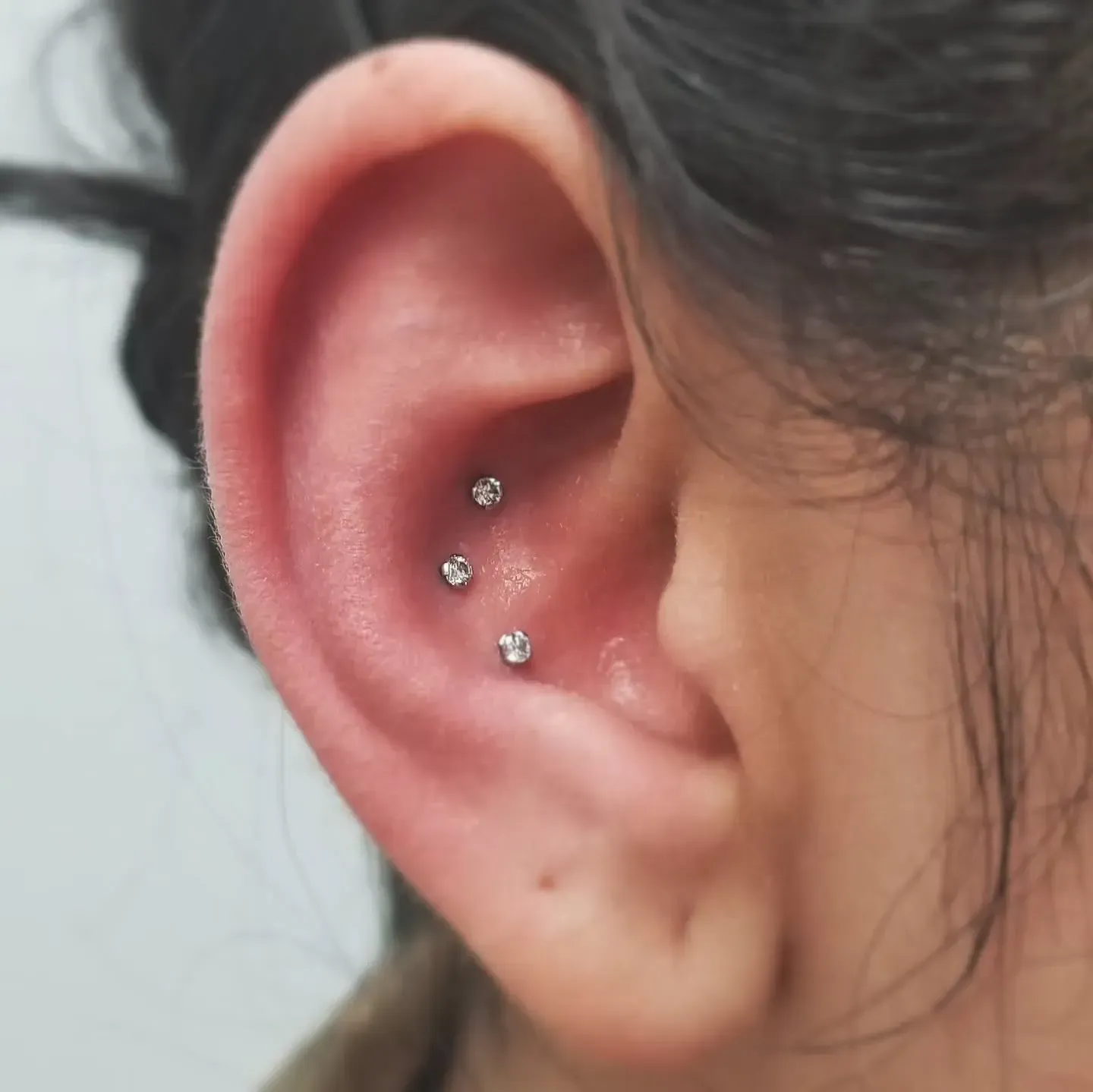 A close up of a woman 's ear with three piercings.